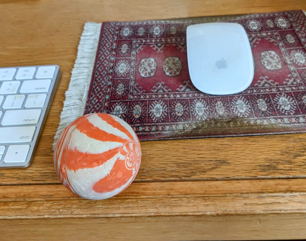 Orange and white hard rubber ball sitting on my desk between my keyboard and my mouse pad.