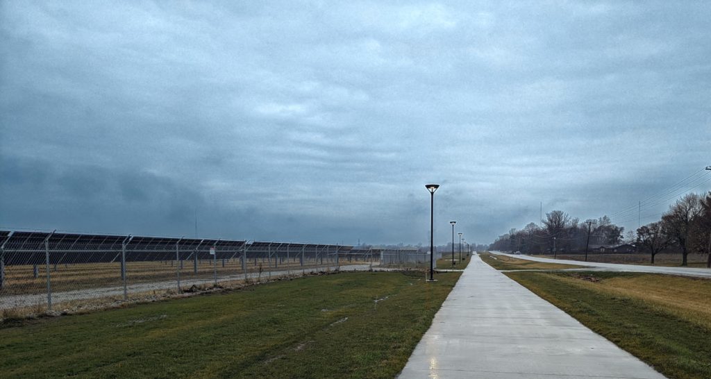 Looking up a multi-use path past a solar farm, under a stormy sky