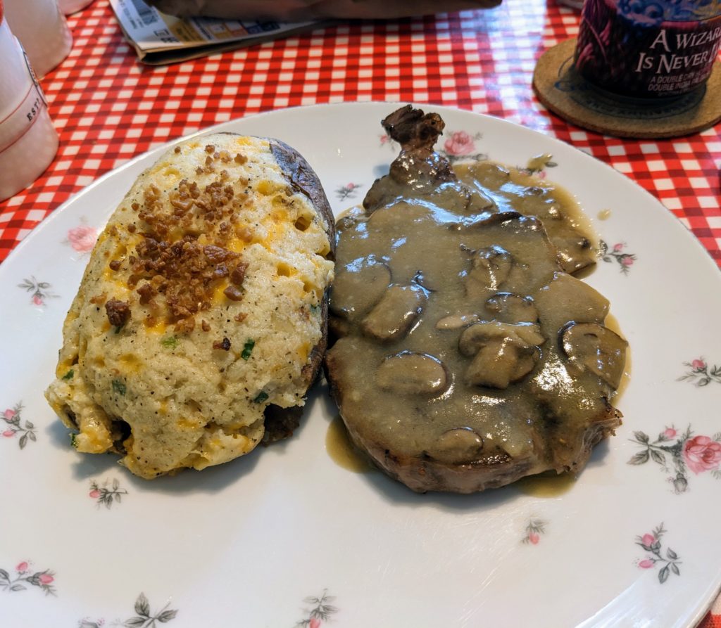 Twice-baked potato next to a steak covered with mushroom gravy, with a beer can next to the plate
