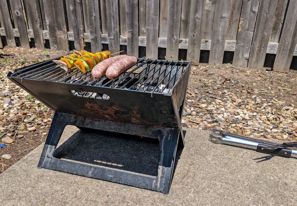 A charcoal grill with two skewers of veggies and two bratwurst