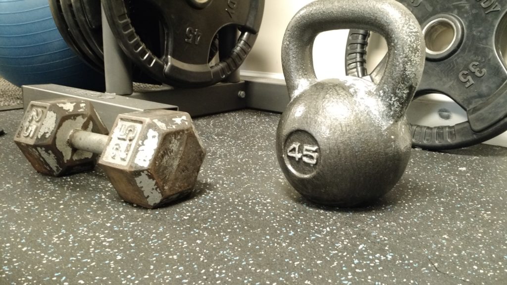 25 lb dumbbell and 45 lb kettlebell in front of some weight plates.