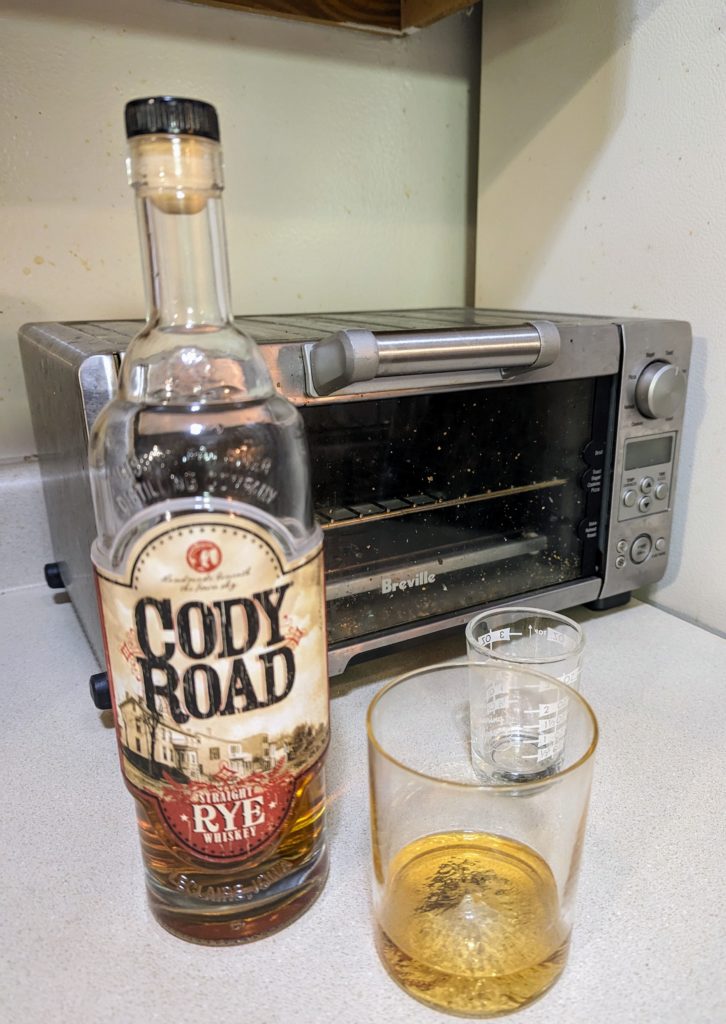 A bottle of Cody Road Rye in front of a pour of the whiskey in a whiskey peaks glass