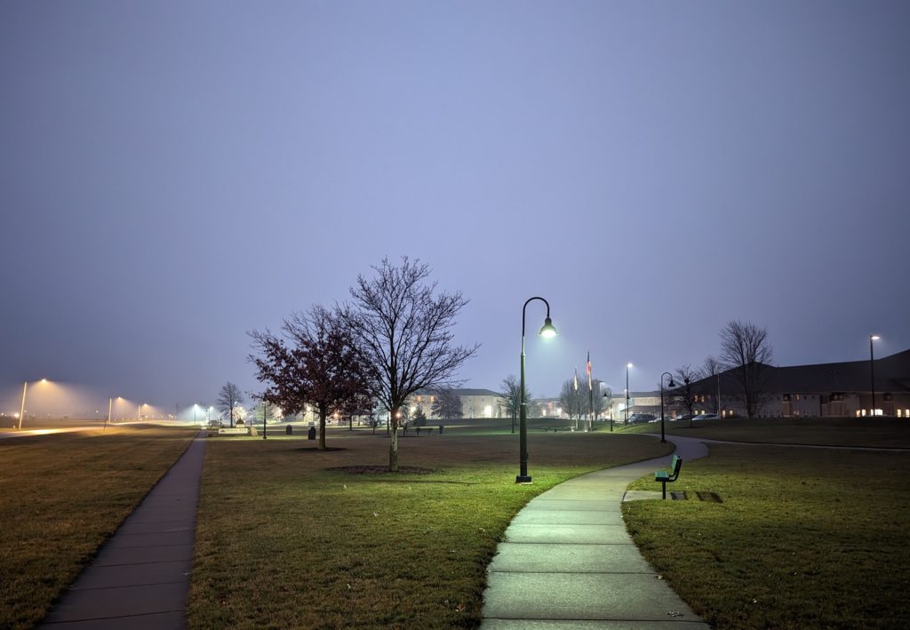 A street lamp illuminates the fog over a park bench