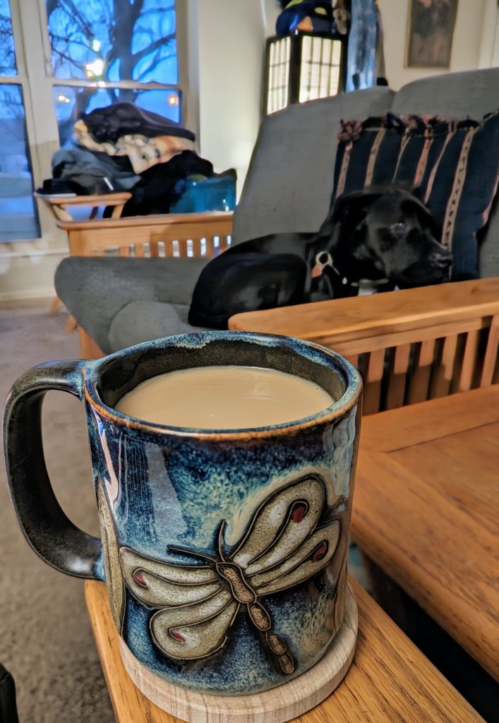 A full mug of coffee, with a dog visible beyond