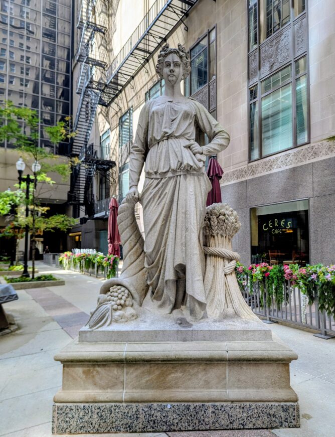 A large statue of a woman with fruit and grain standing in a public square