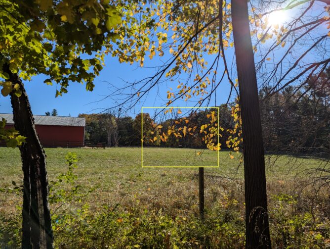 A pasture with a barn, with a barely visible horse in the distance, highlighted with a yellow rectangle