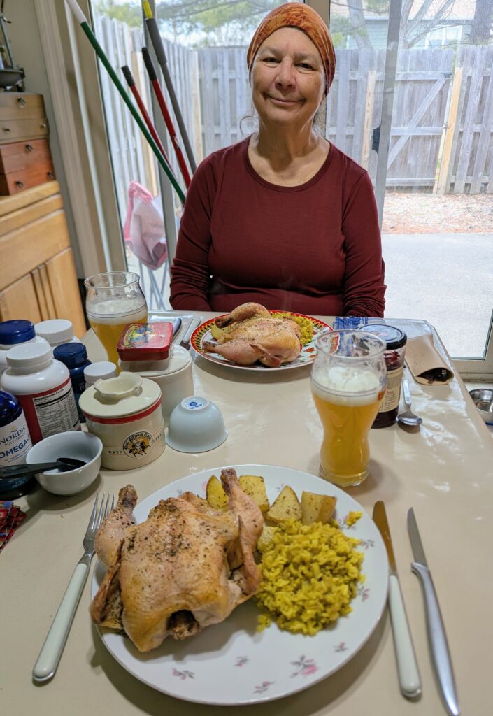 In the foreground is a plate with a rock cornish game hen, rice, and roasted potatoes, with a woman sitting across the table with the same meal served