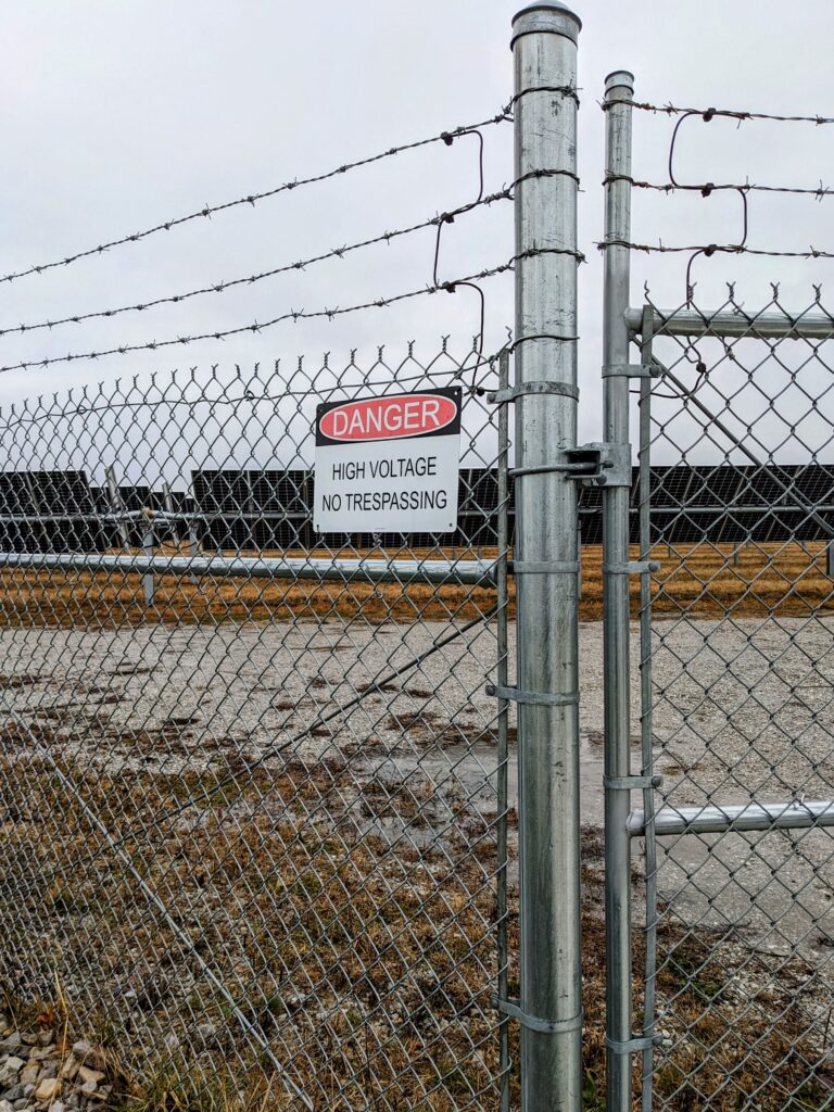Border fence with barbed wire at the top and a sign warning