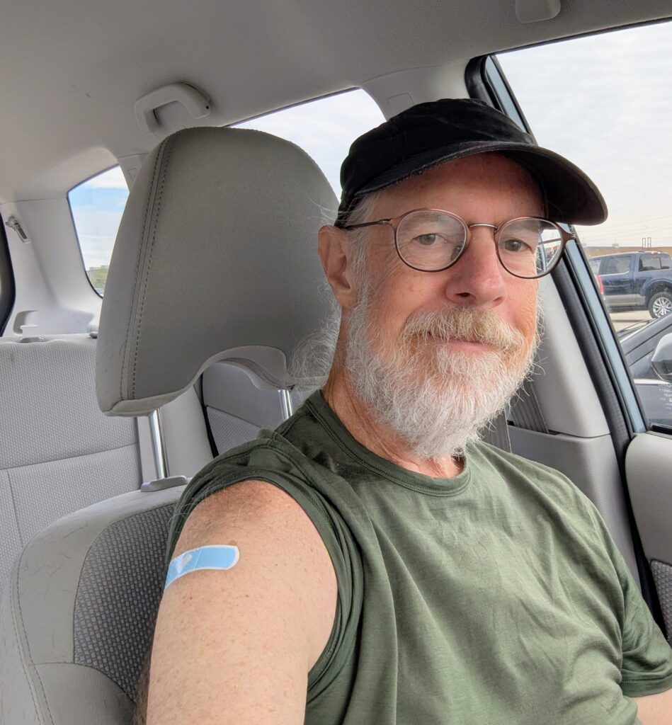 A selfie of me in a car, showing a bandaid on my upper right arm